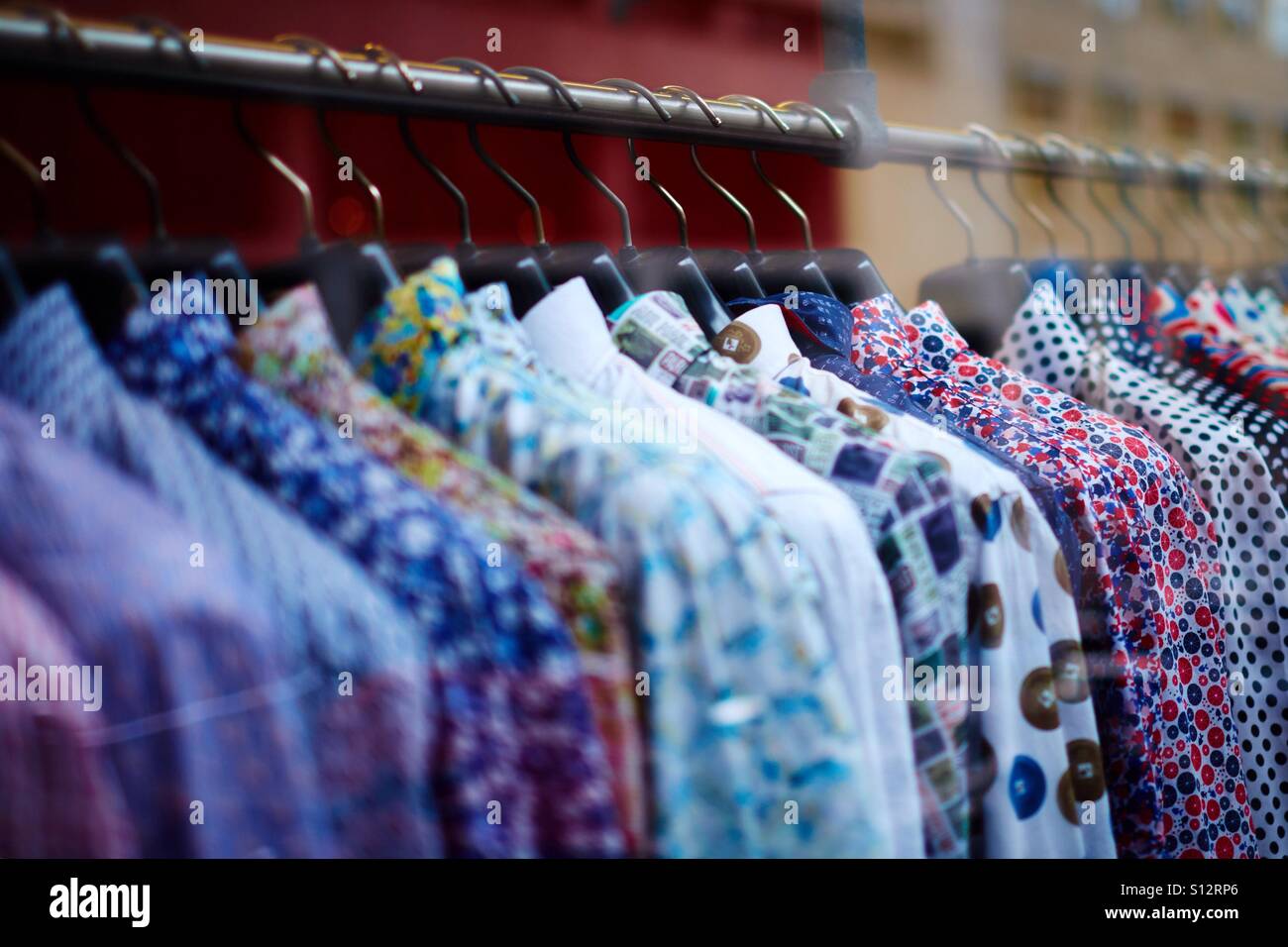 Close-up of a shop rail full of colourful patterned shirts for sale. Stock Photo