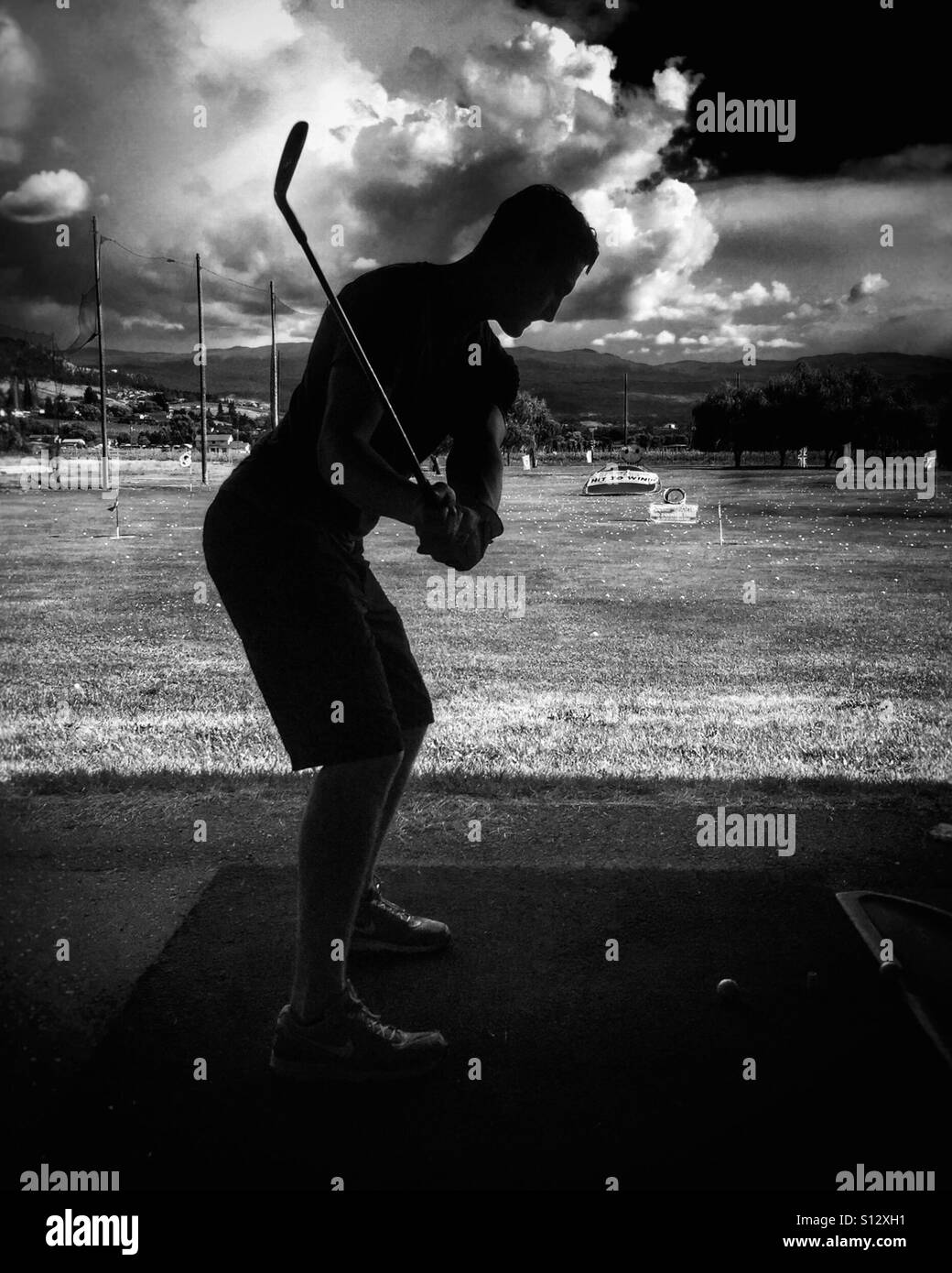 Silhouette of young man hitting golf balls at a driving range. In black and white - Smartphone Captured Stock Image