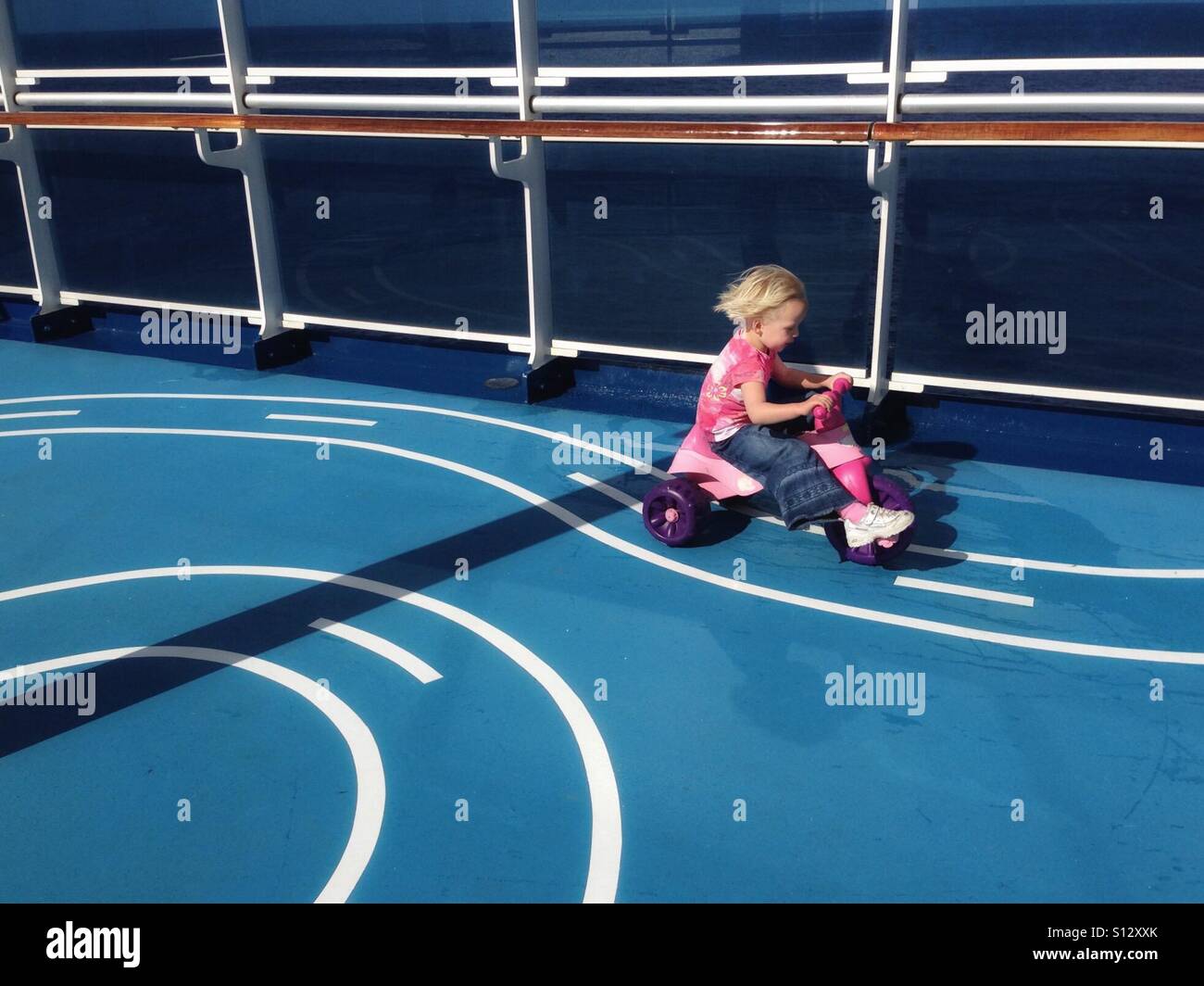 A girl races a tricycle around a track on a cruise ship. Stock Photo