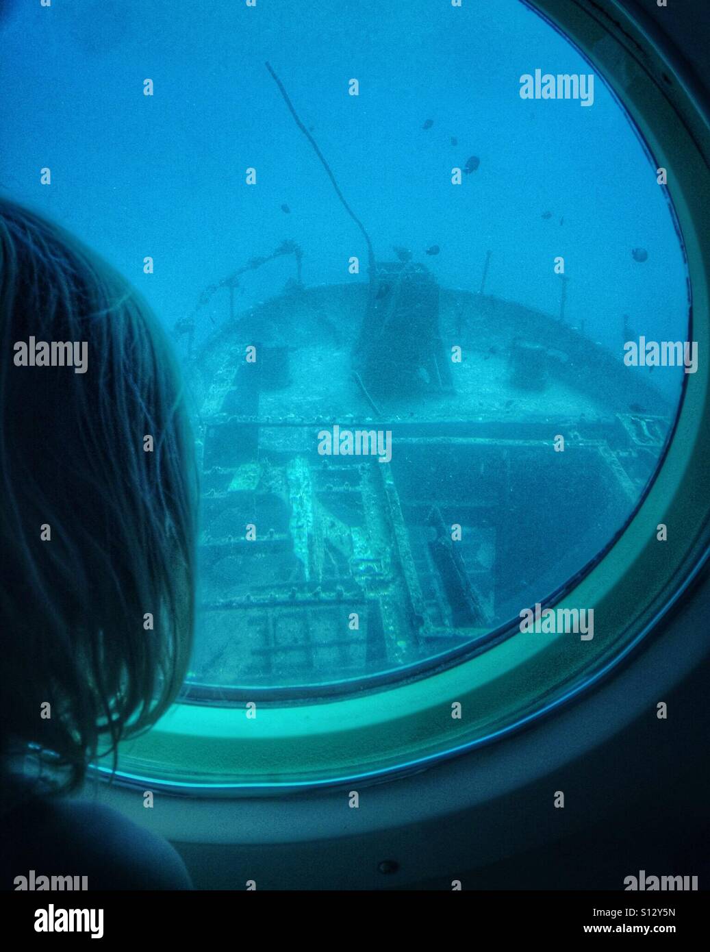 A girl views a sunken ship through the porthole of a submarine. Stock Photo