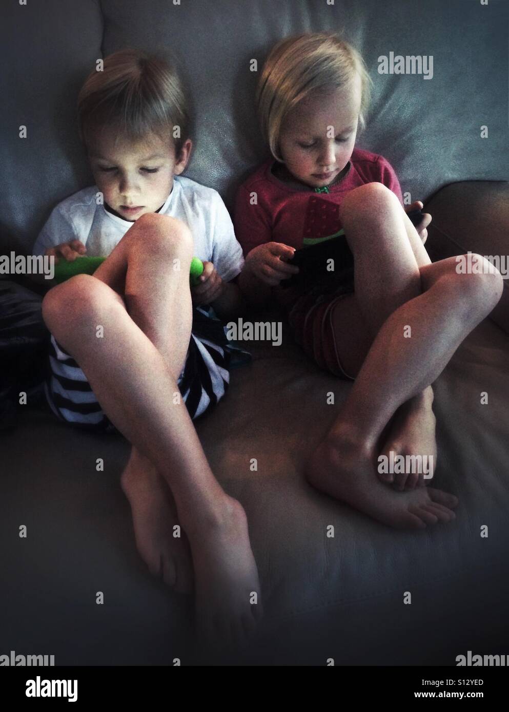 Two children focus intently on their tablets. - Smartphone Captured Stock Image