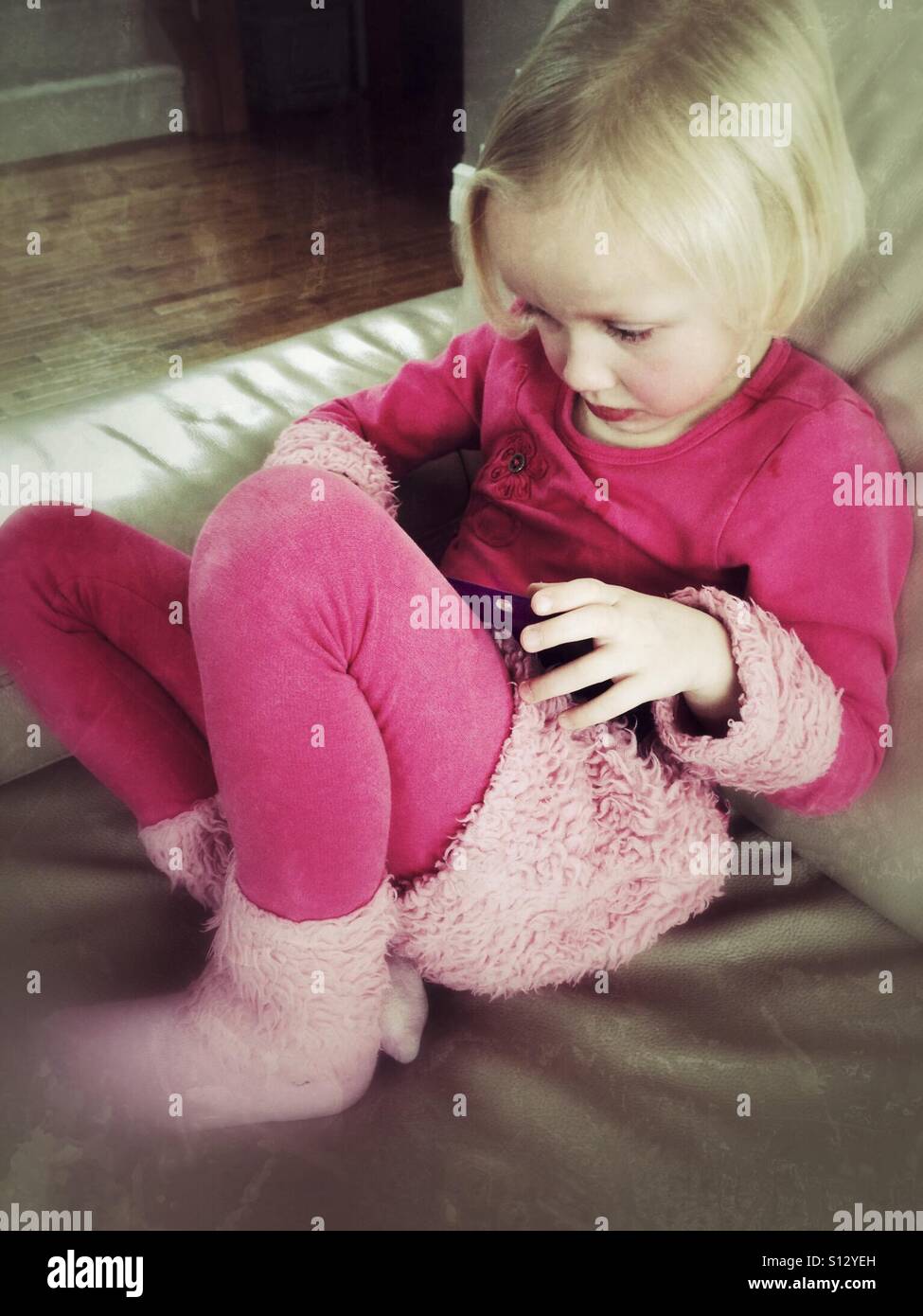 A girl curled on a couch plays with her tablet. - Smartphone Captured Stock Image