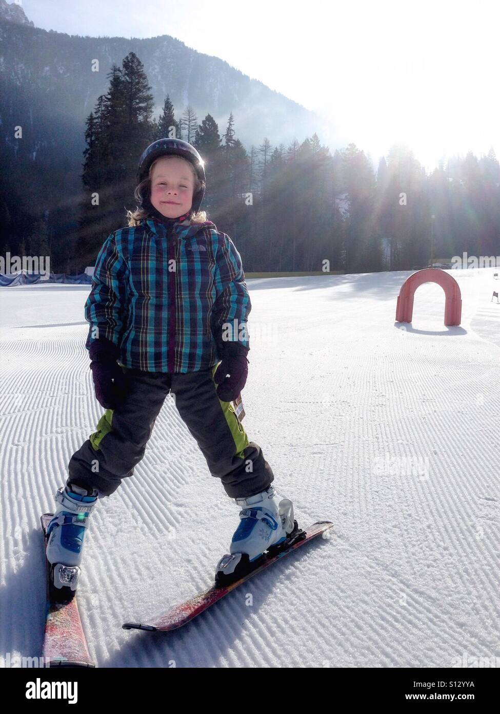 Glowing in the morning sun, a helmeted girl learns to ski. - Smartphone Captured Stock Image