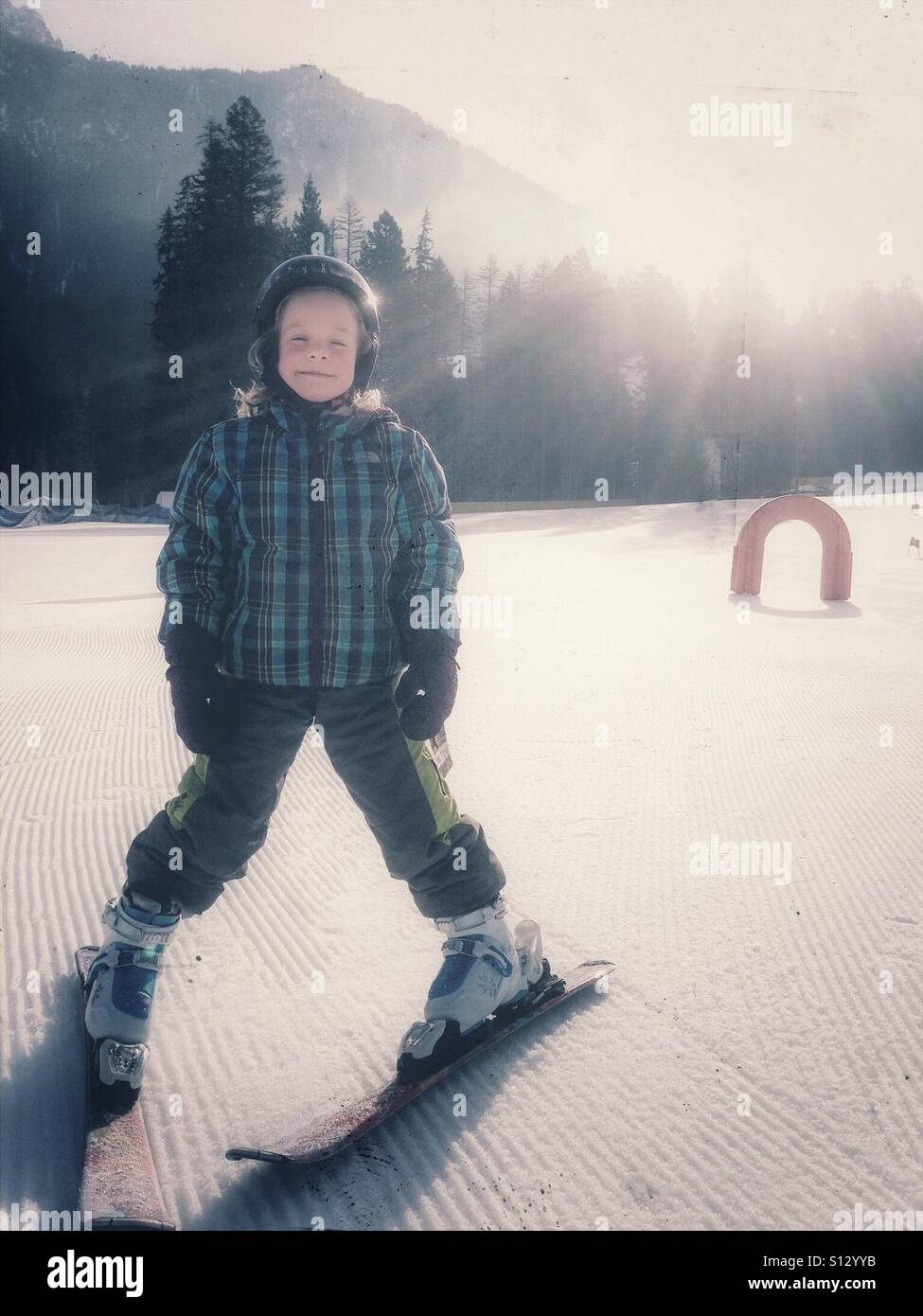Glowing in the morning sun, a happy girl learns to ski. - Smartphone Captured Stock Image