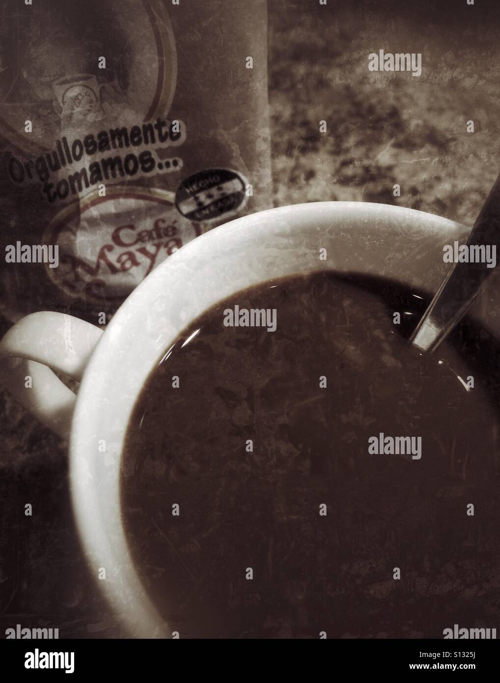 A closeup of a full coffee cup with a spoon and part of the packaging behind. - Smartphone Captured Stock Image