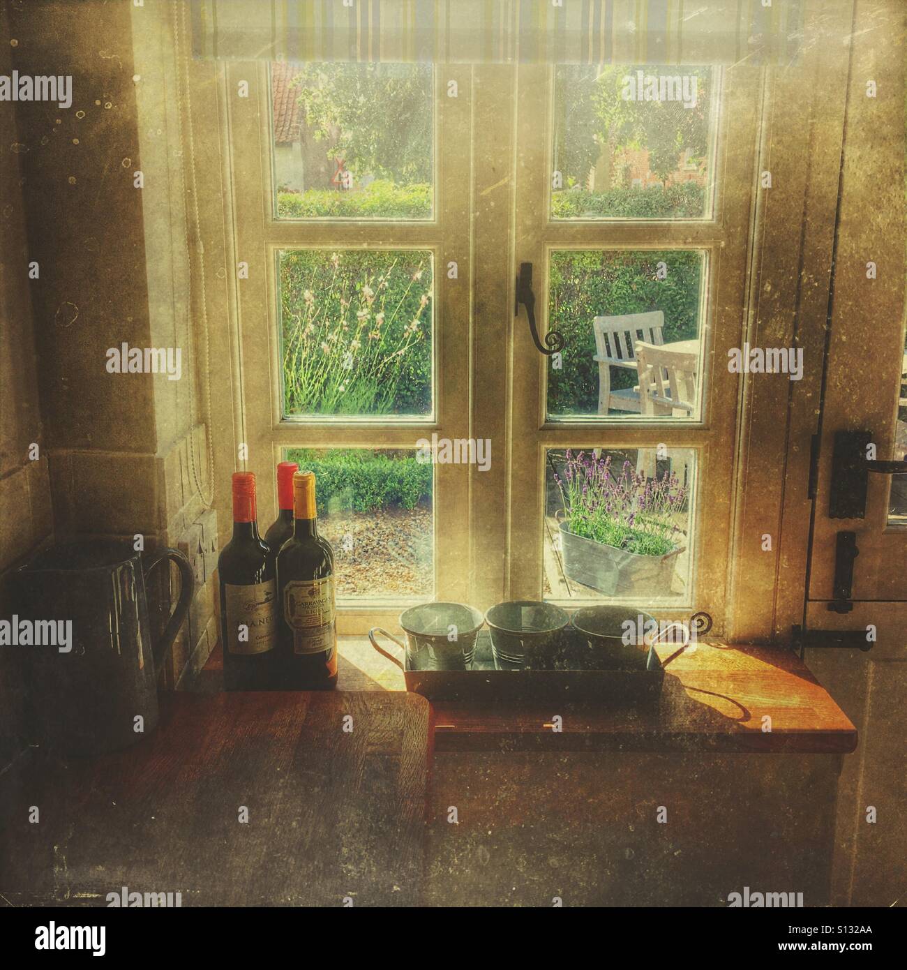 Rustic kitchen interior with vintage cookware and red wine on a wooden worktop, looking out through a window to a country garden. - Smartphone Captured Stock Image