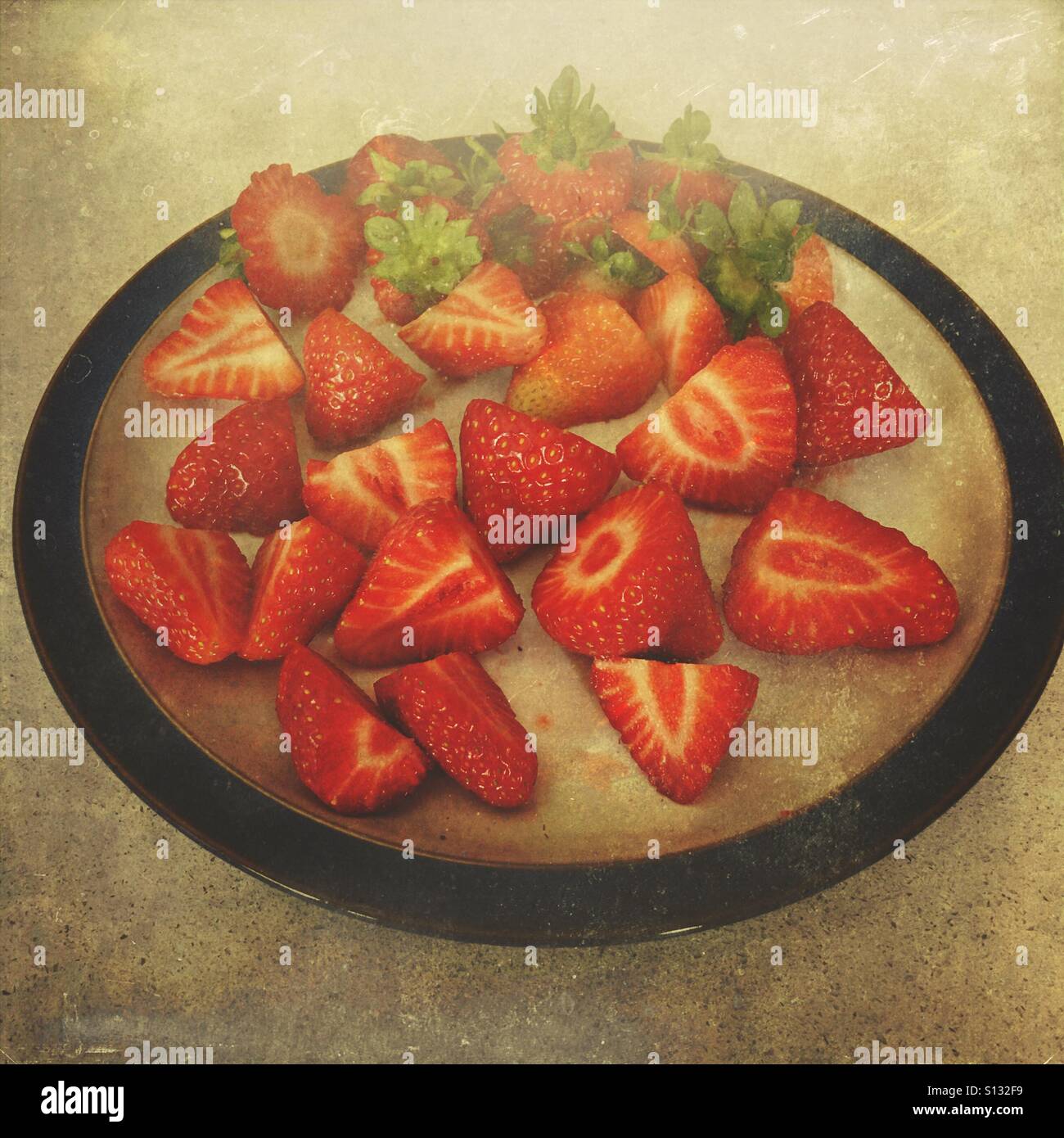 Overhead still life of sliced fresh strawberries arranged on a ceramic plate, styled with textured, artistic processing for editorial food and lifesty - Smartphone Captured Stock Image