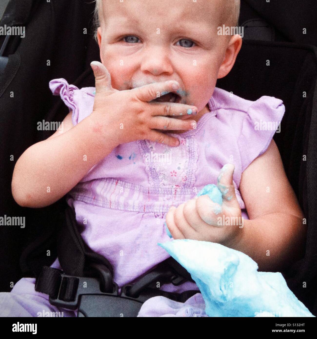 A toddler pushes blue cotton candy into her mouth. Stock Photo