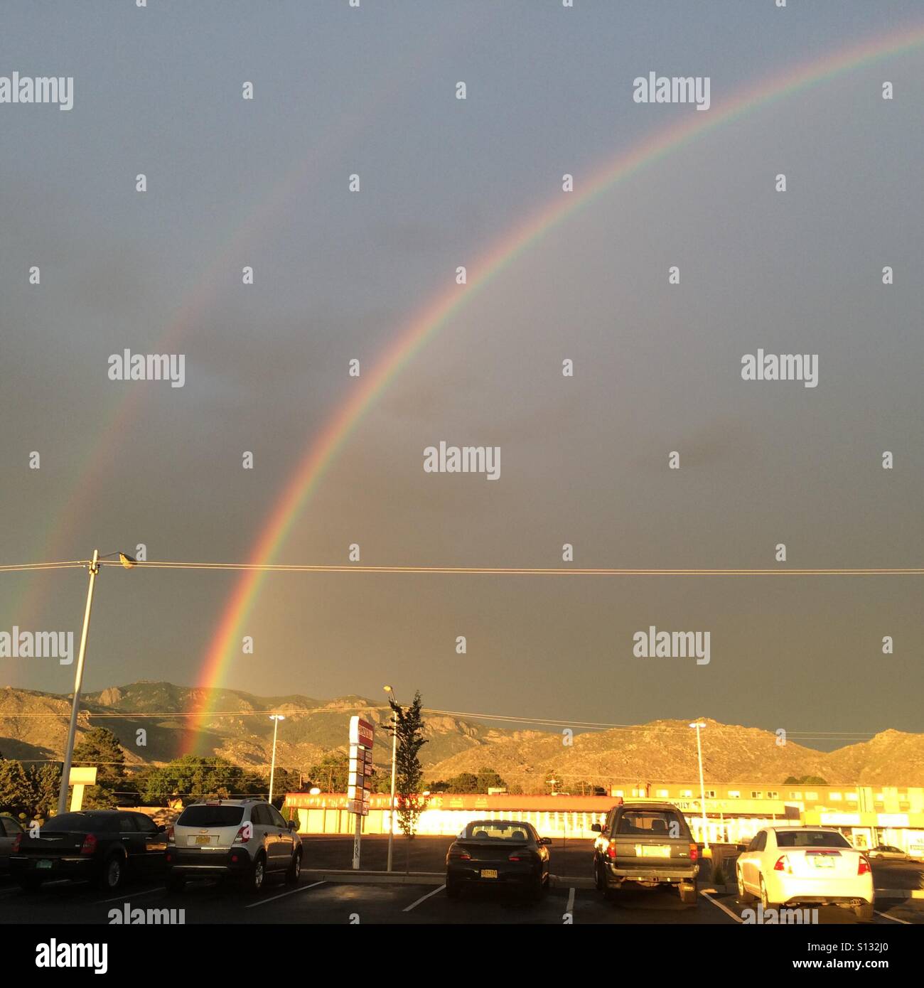 Double rainbow rising above a parking lot. Stock Photo