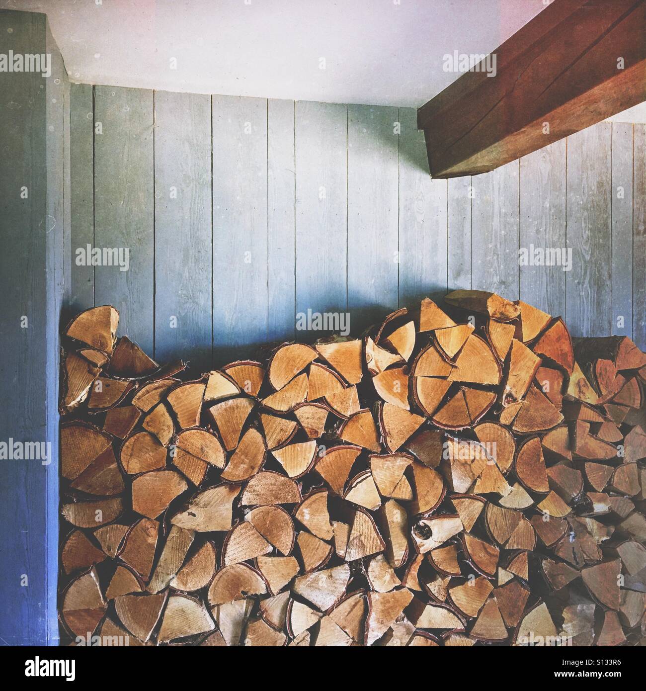 Stacked firewood logs against a wooden interior wall, creating a natural texture background with copy space, evoking rustic warmth & sustainability. - Smartphone Captured Stock Image