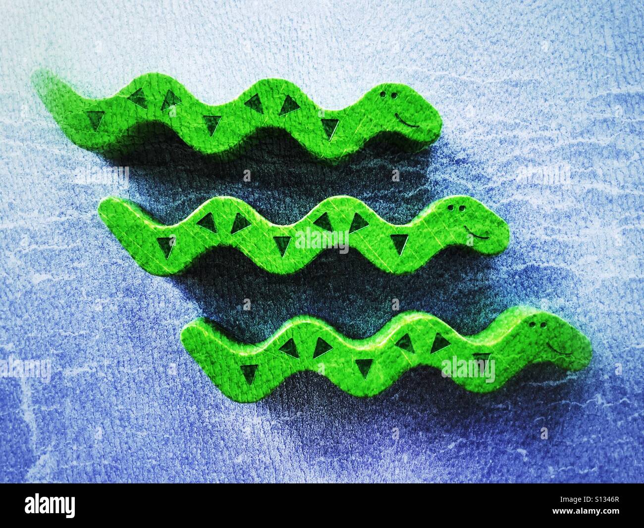 Three wooden toy snakes on a blue background. 3 of 3 in a series. Stock Photo