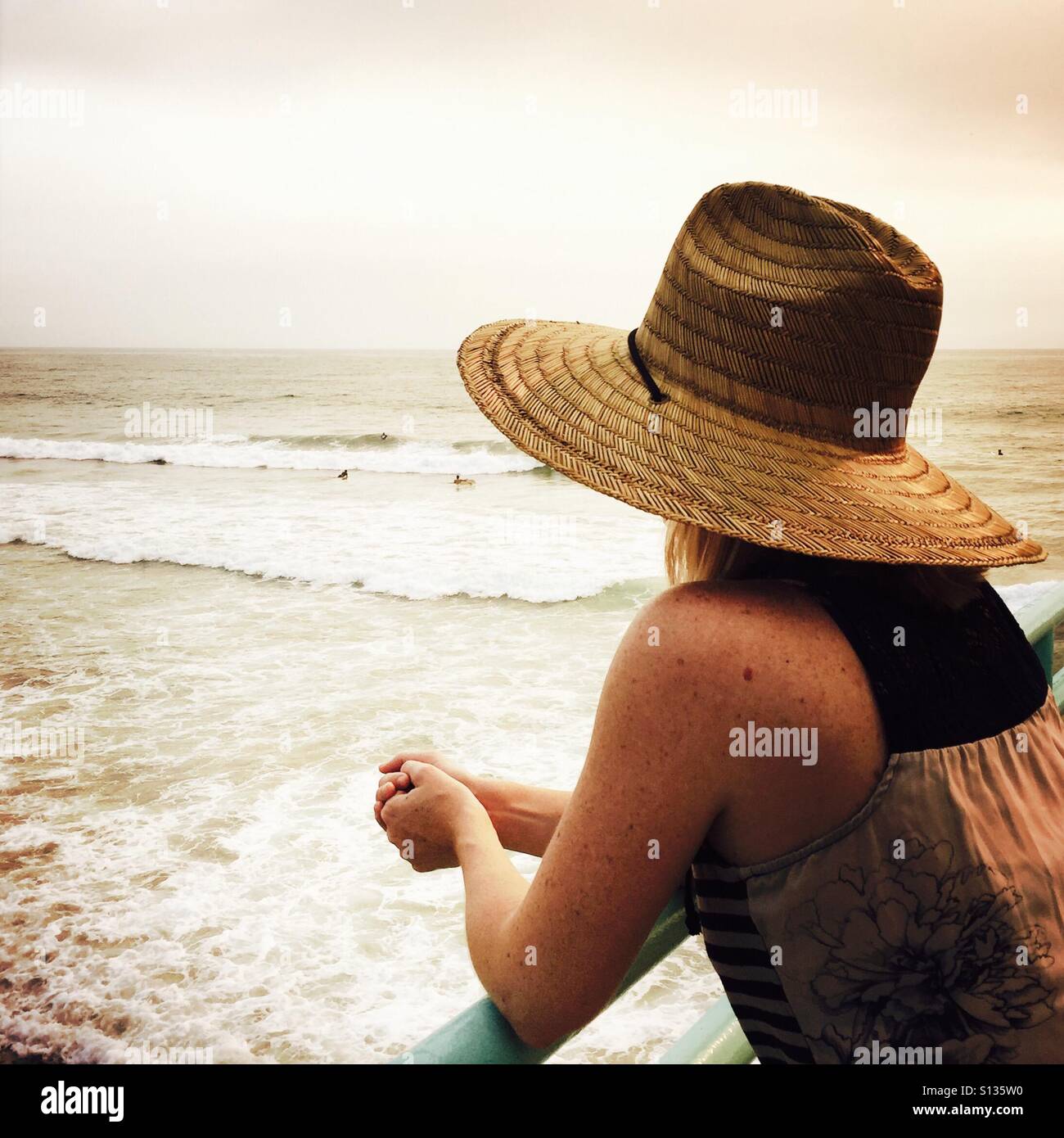 A young women in a hat looks out to the ocean on the Manhattan Beach pier. Manhattan Beach, California USA. Stock Photo