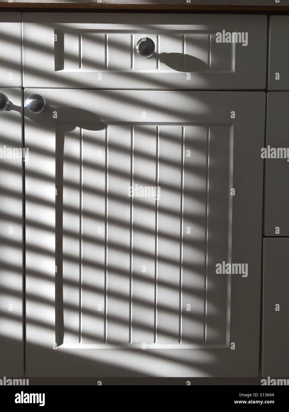 Diagonal shadows across a white bead board cupboard door. - Smartphone Captured Stock Image