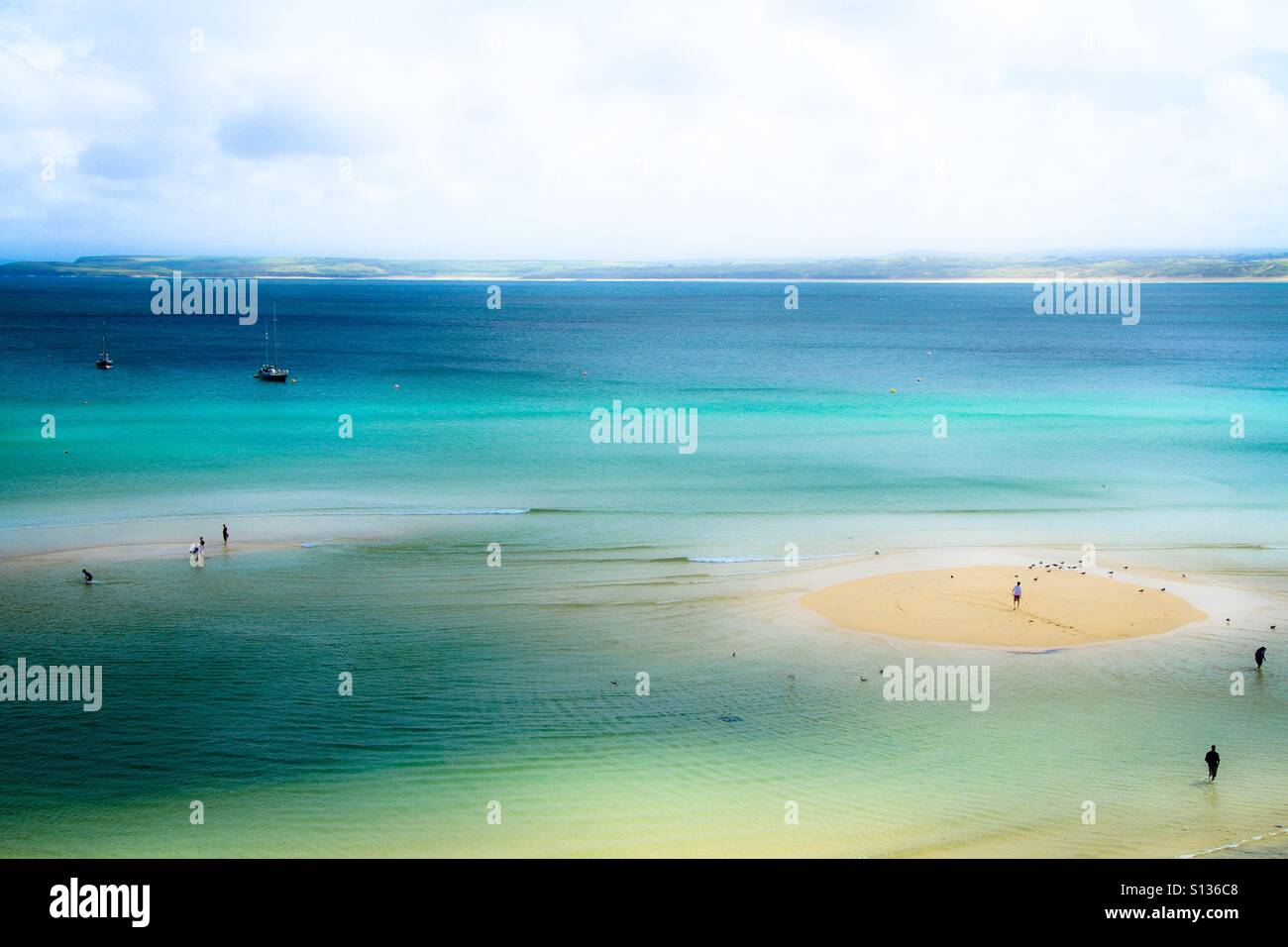 A dreamy beach from above with sand banks and holidaymakers scattered around and enjoying the emerald green ocean. Stock Photo
