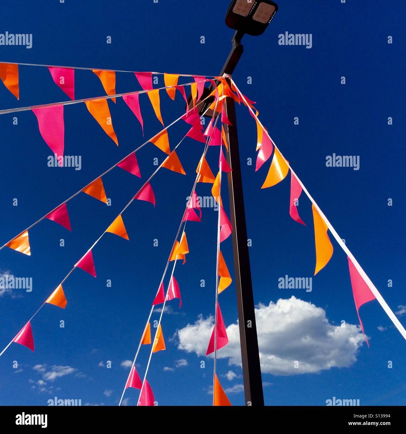 Flags upon a light pole stand in front of a blue sky containing a few clouds. Stock Photo