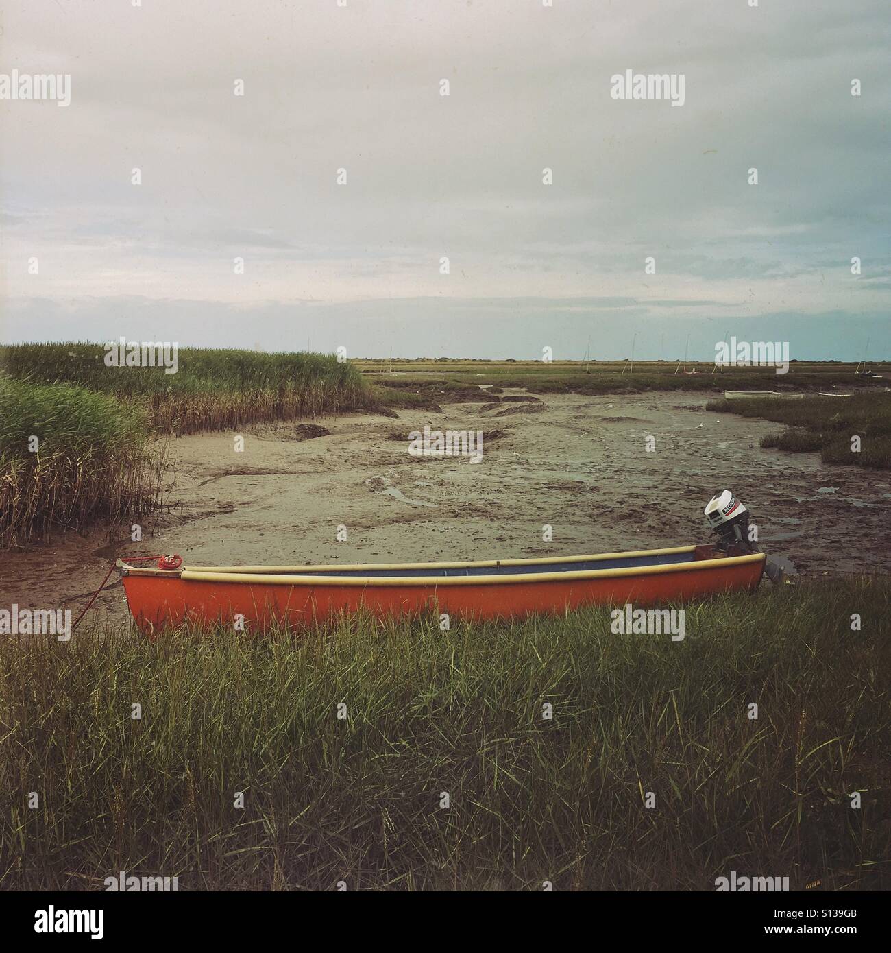 Orange boat lying in mud flats and salt marshes, at Brancaster Staithe, Norfolk, England, UK. - Smartphone Captured Stock Image