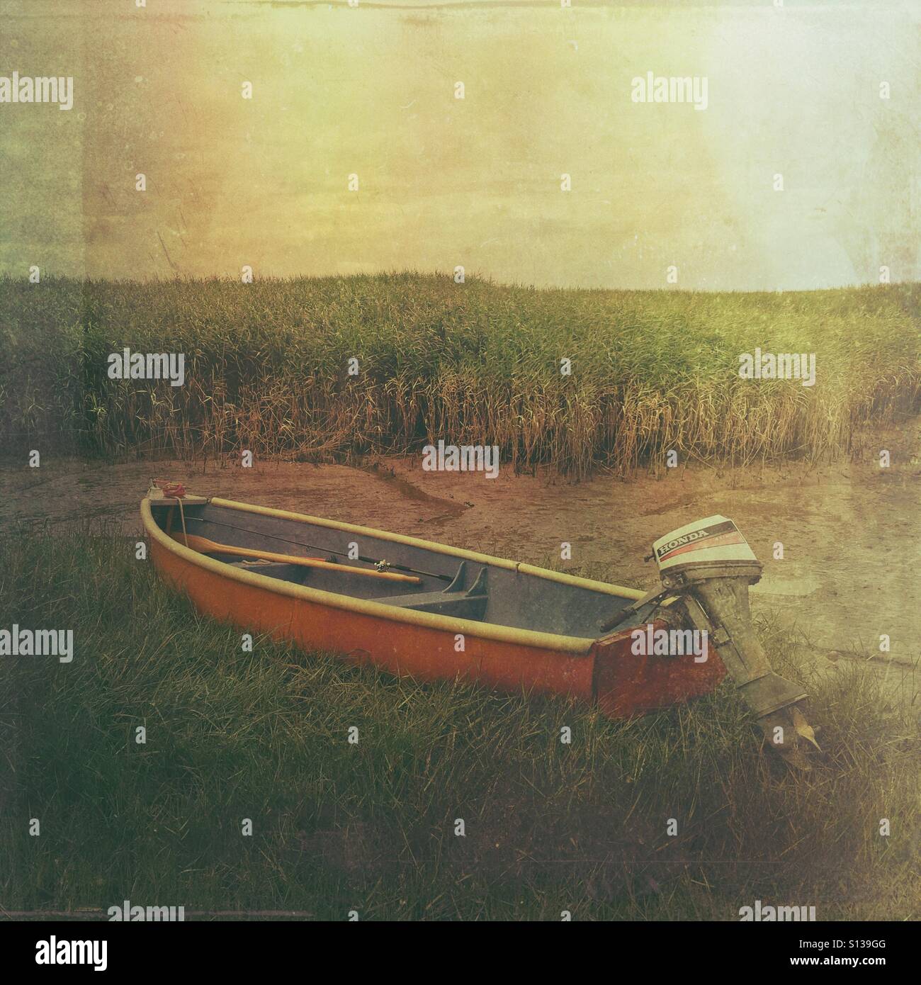 Orange boat lying in mud flats and salt marshes, at Brancaster Staithe, Norfolk, England, UK. - Smartphone Captured Stock Image