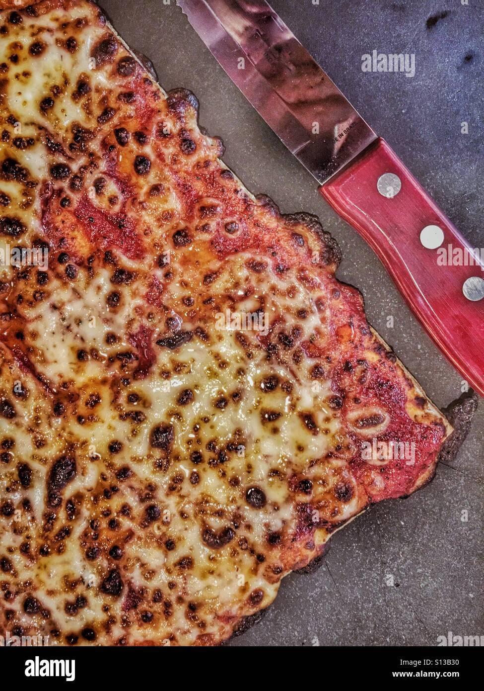 Freshly baked cheese pizza on a stone slate with a knife - Smartphone Captured Stock Image
