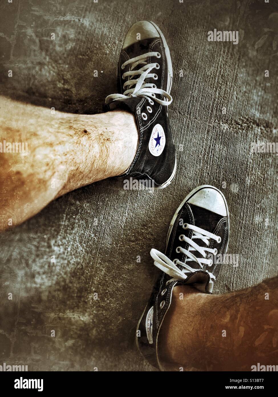 Man's hairy legs with a pair of Converse tennis shoes Stock Photo