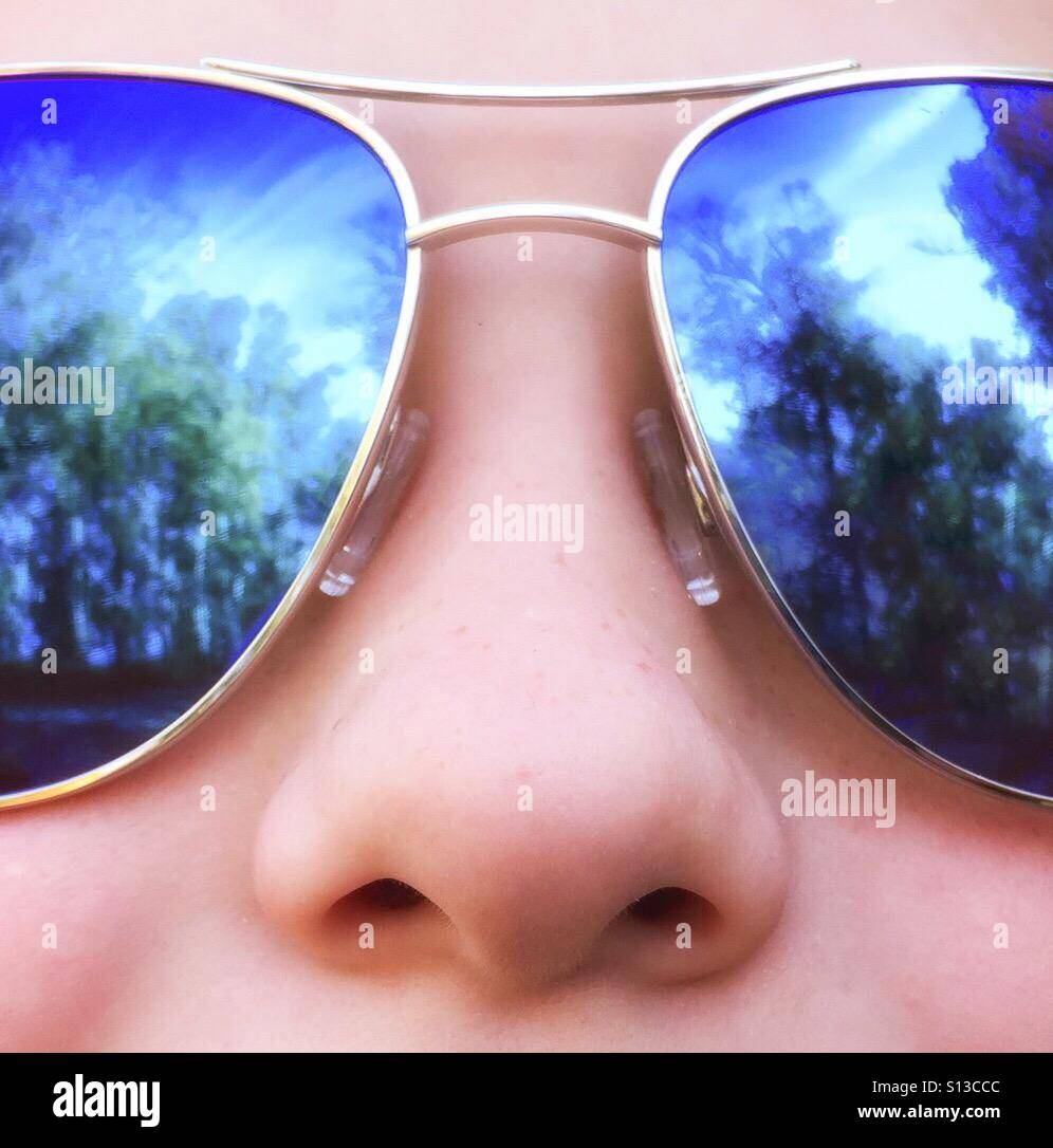 A closeup of a freckled girl wearing mirrored sunglasses outdoors. - Smartphone Captured Stock Image