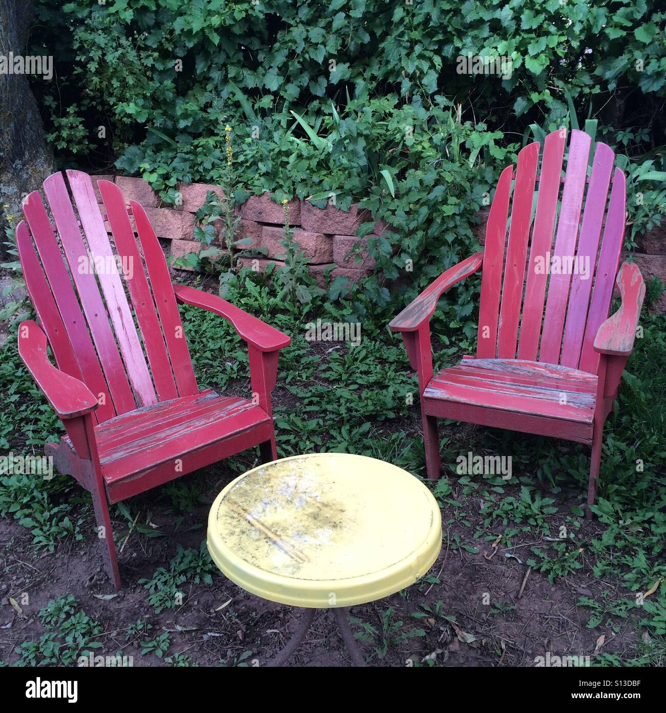 Two red Adirondack chairs sit in front of a garden table. Stock Photo