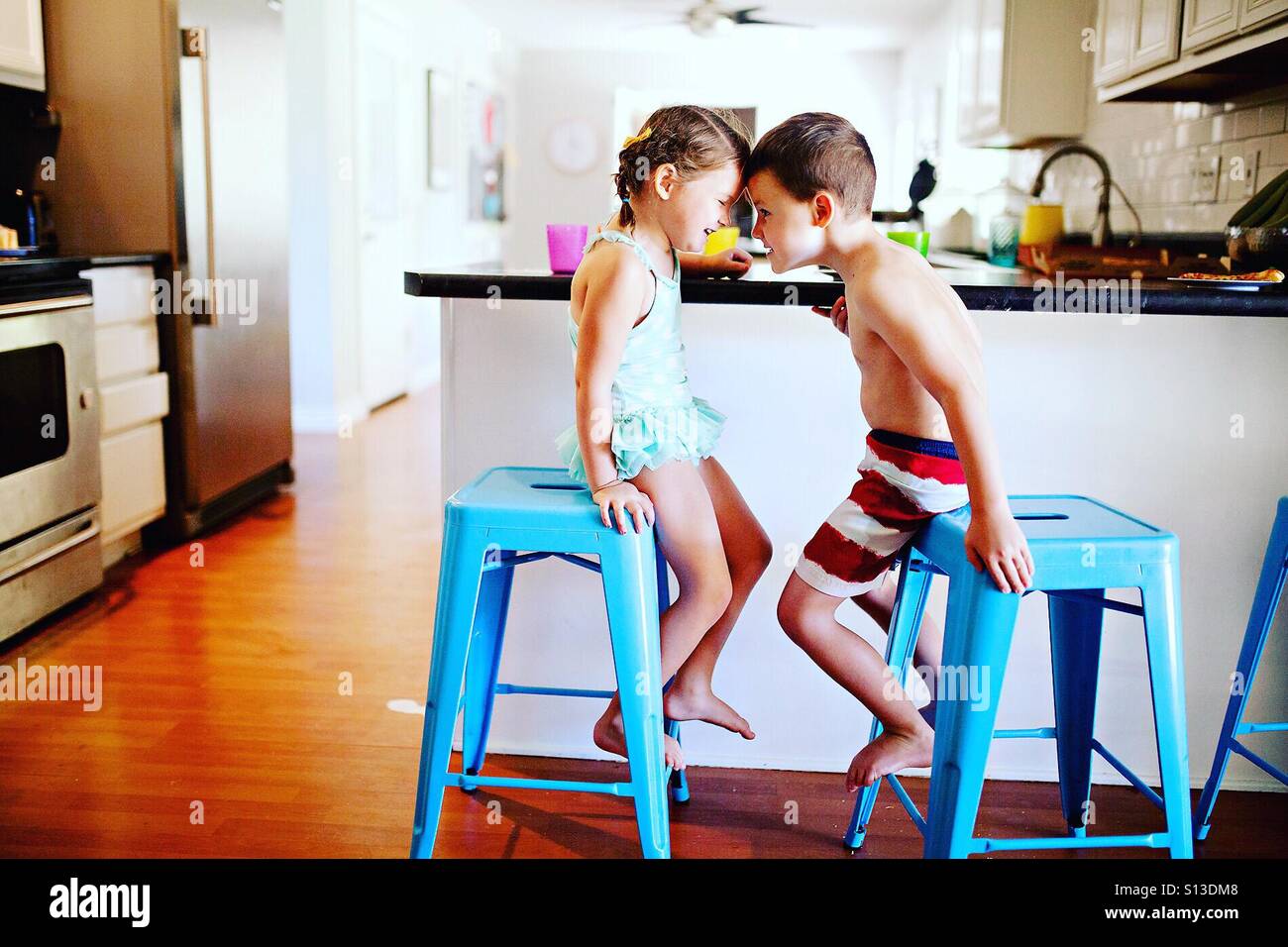 Two children in swim suits being silly at meal time at home in modern kitchen Stock Photo