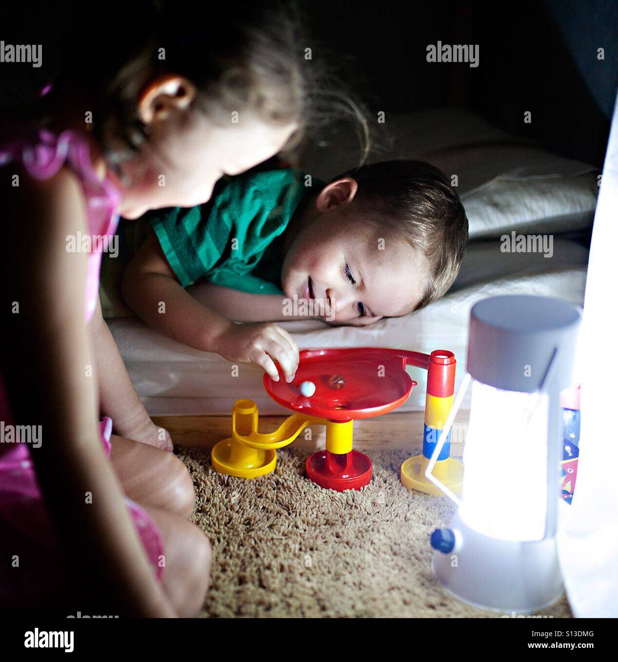 Toddler and your girl play with a marble run toy at bedtime by lamp light Stock Photo
