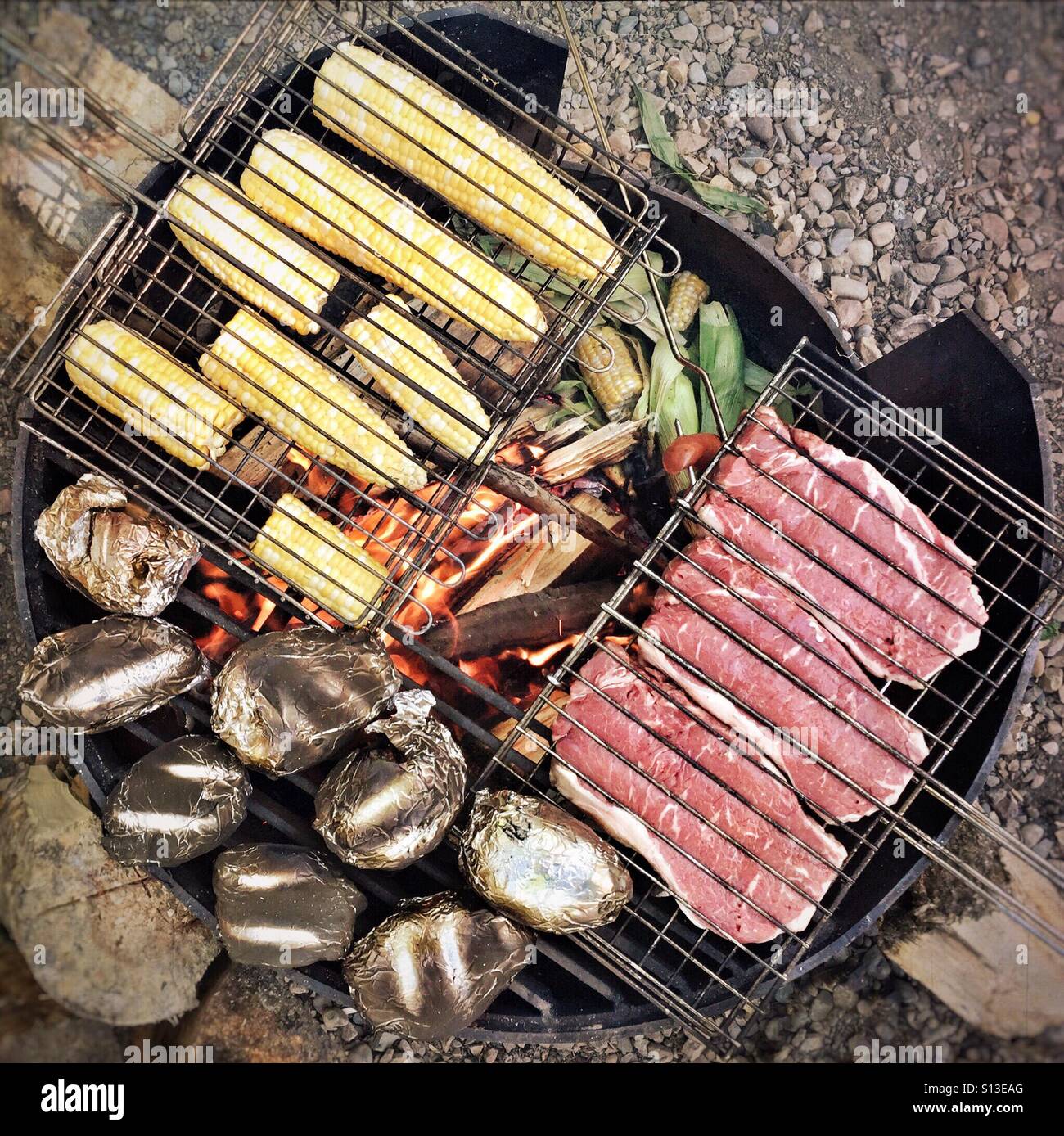 Steak corn and potatoes cook over an open fire. Stock Photo