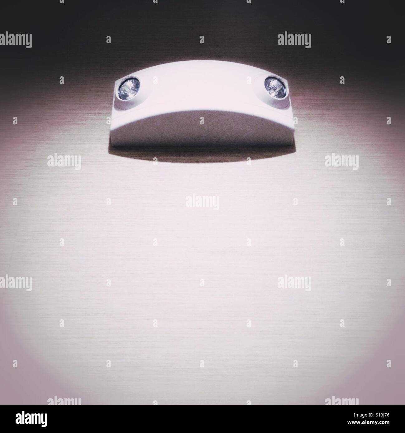 Pareidolia is the human propensity to see faces in inanimate objects. An emergency light looks down from a wall. - Smartphone Captured Stock Image