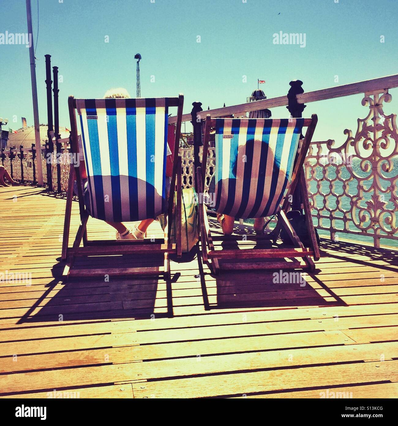 Sunbathers in deckchairs on a pier in Brighton England UK - Smartphone Captured Stock Image