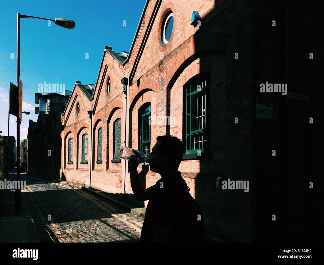 Silhouette of  a man drinking water from a bottle in East London - Smartphone Captured Stock Image