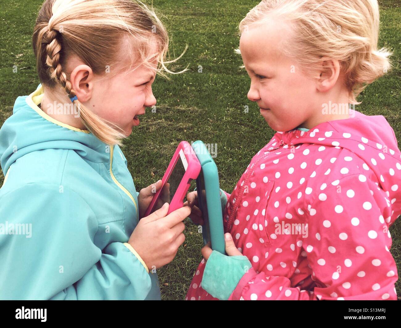 Two girls battle over their tablets. - Smartphone Captured Stock Image