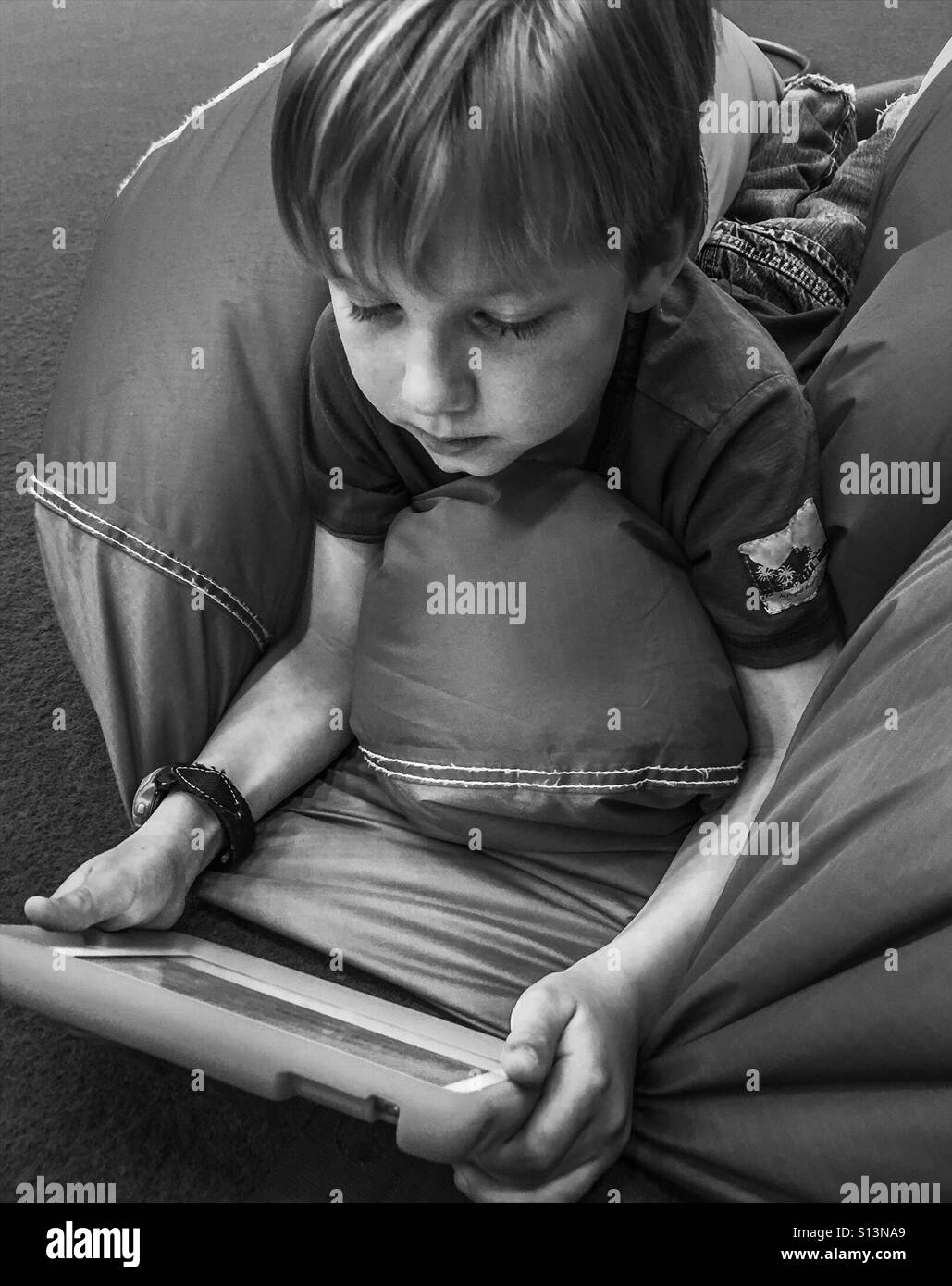 A boy lying on his stomach plays on a tablet. Stock Photo