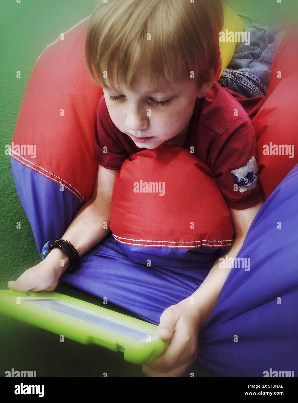 A boy lying on his stomach on a deflated ball plays on his mobile device. - Smartphone Captured Stock Image