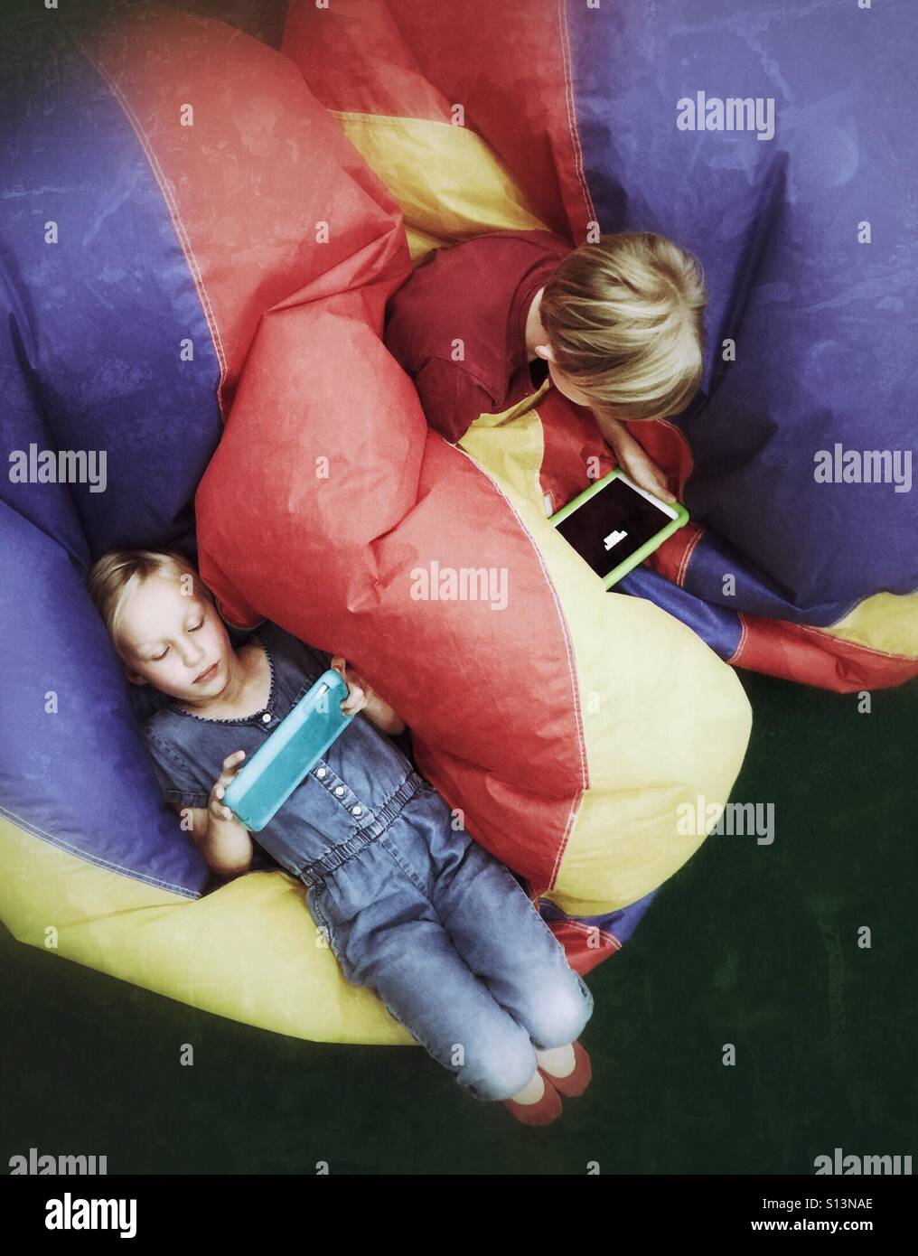 An aerial view of two children playing on their mobile devices while relaxing on partially deflated toy balls. Stock Photo