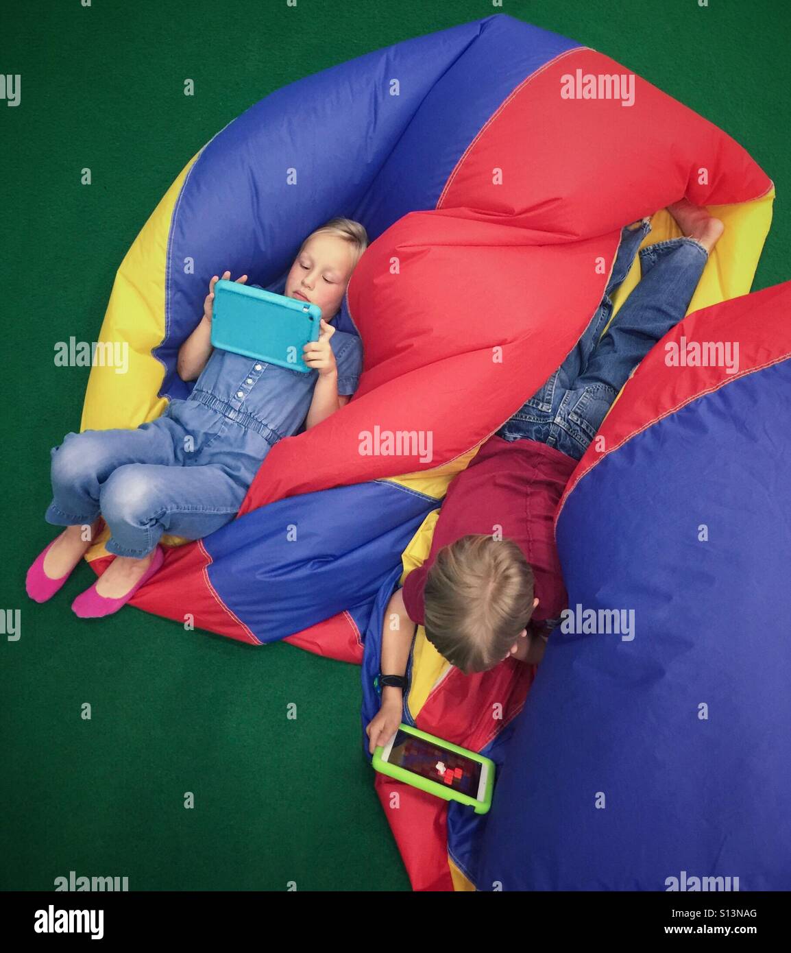 An aerial view of a pair of siblings playing on their tablets. - Smartphone Captured Stock Image