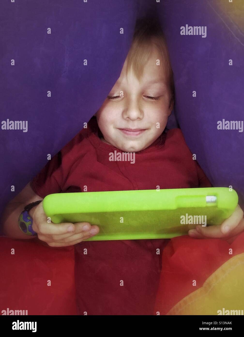 A comfortable, content boy plays with his tablet while laying on a partially deflated ball. - Smartphone Captured Stock Image
