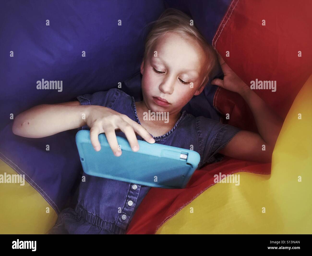 A child lays on a deflating multi-coloured ball to play games on a tablet. - Smartphone Captured Stock Image
