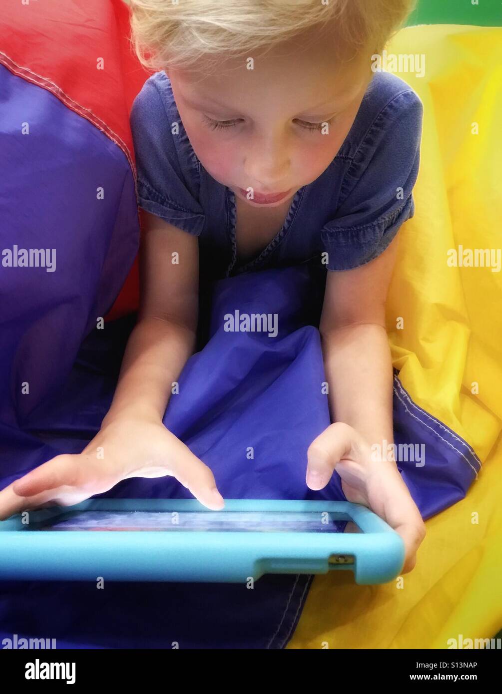 A child laying on her stomach on a deflating ball plays a game on her tablet. Stock Photo