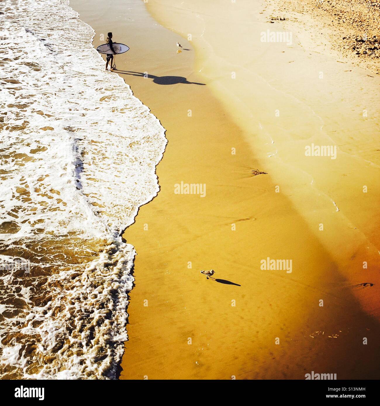 A male Surfer walks up the beach after surfing. Manhattan Beach, California USA. Stock Photo