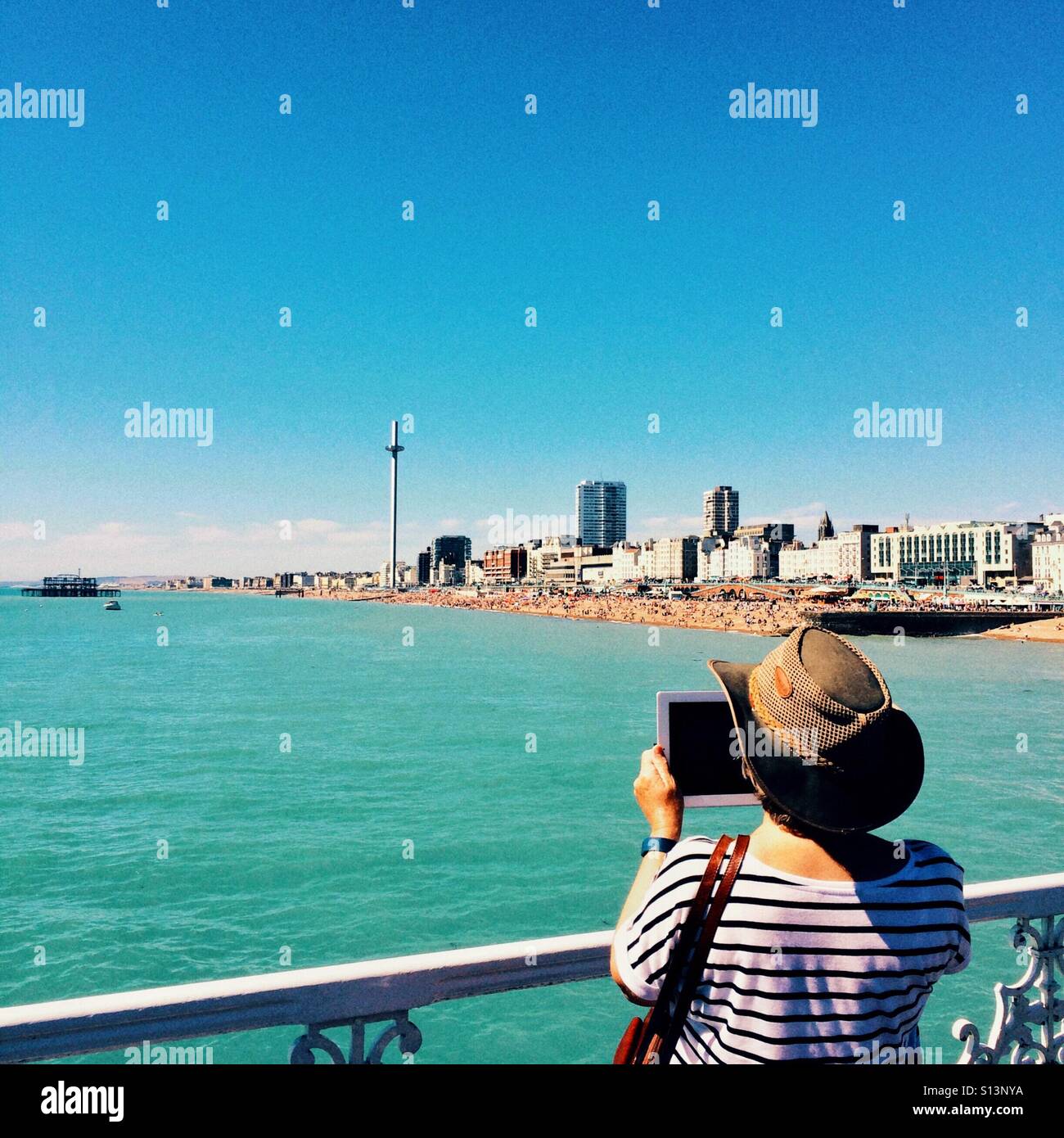 Taking a photo on a tablet on Brighton Pier looking towards the i360 on Brighton seafront - Smartphone Captured Stock Image