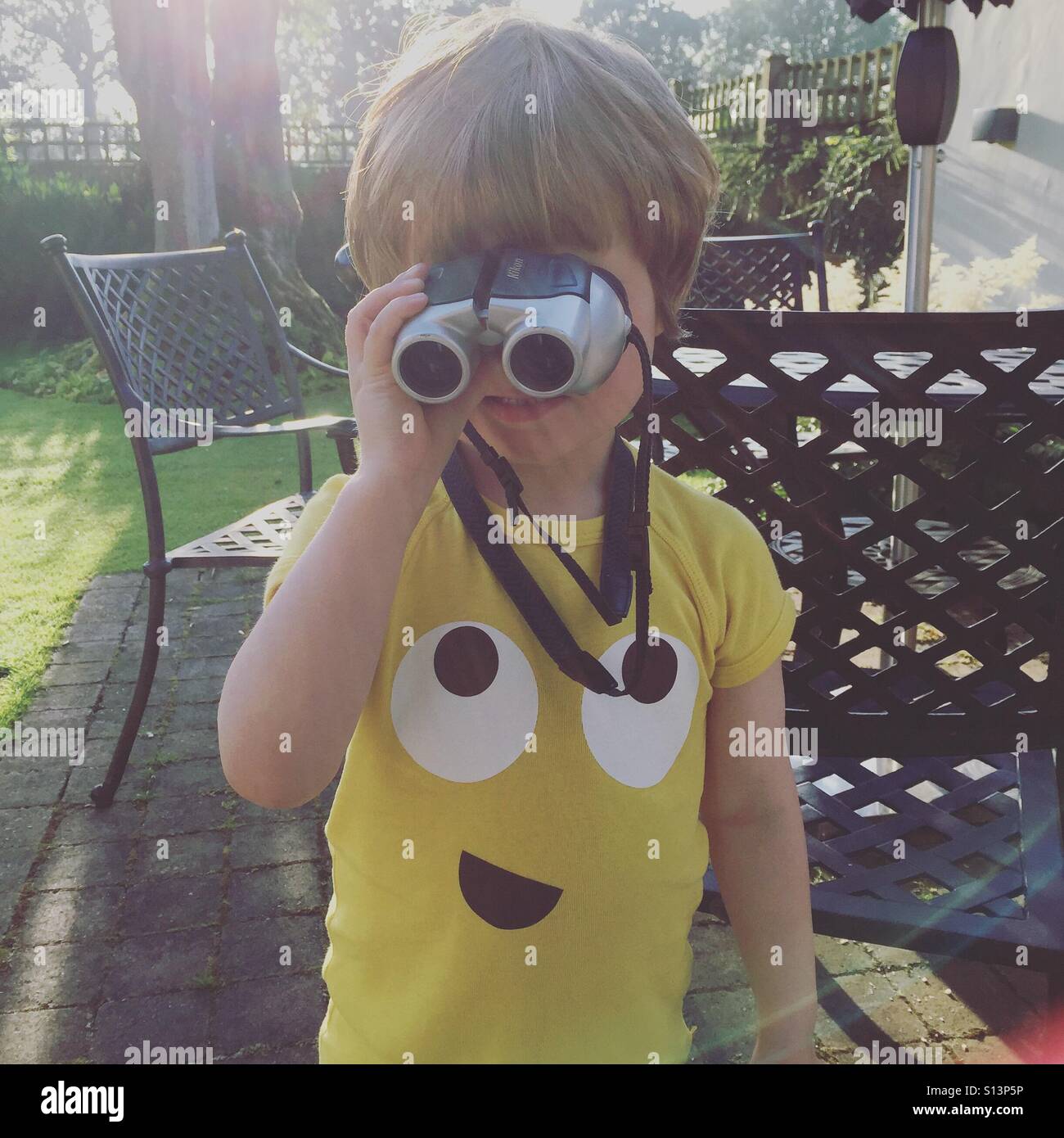 A young boy holds his new bird watching binoculars to his eyes, the wrong way round. Stock Photo