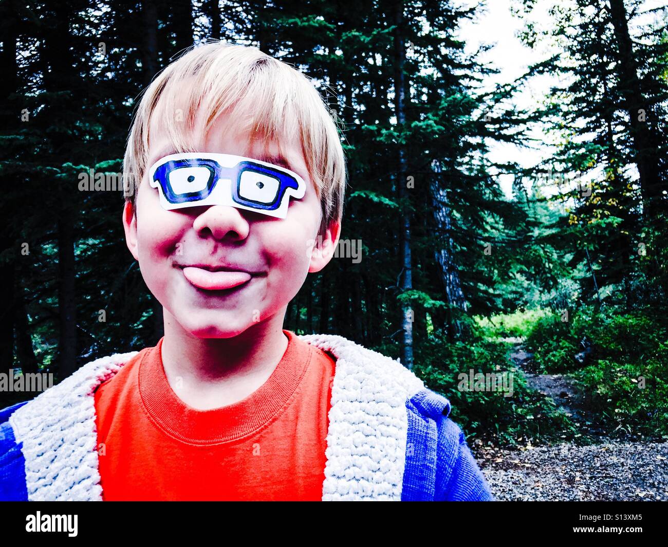A child sticks out his tongue, playing outdoors with pretend glasses stuck over his eyes. - Smartphone Captured Stock Image
