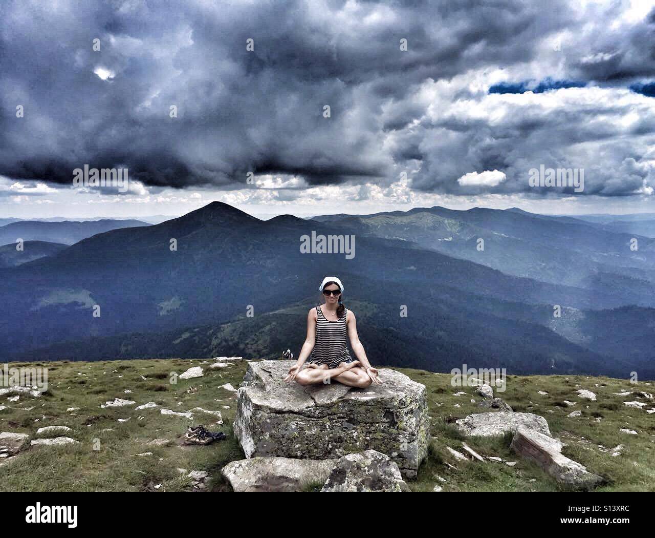 Girl sitting in lotus position in front of the mountains Stock Photo