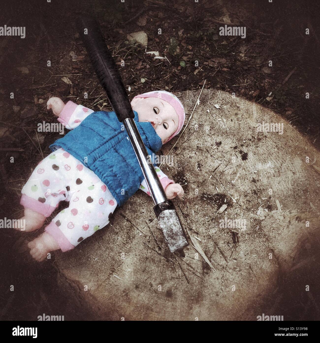 A doll lies outdoors on a stump beneath a hatchet. - Smartphone Captured Stock Image