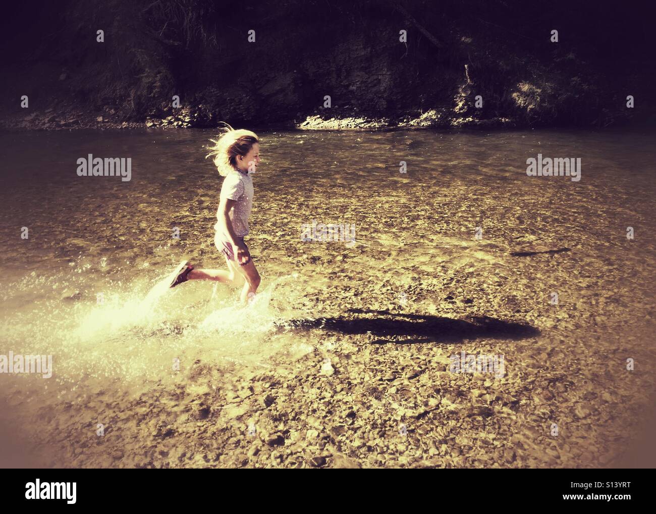 A girl runs through a shallow river, splashing. - Smartphone Captured Stock Image