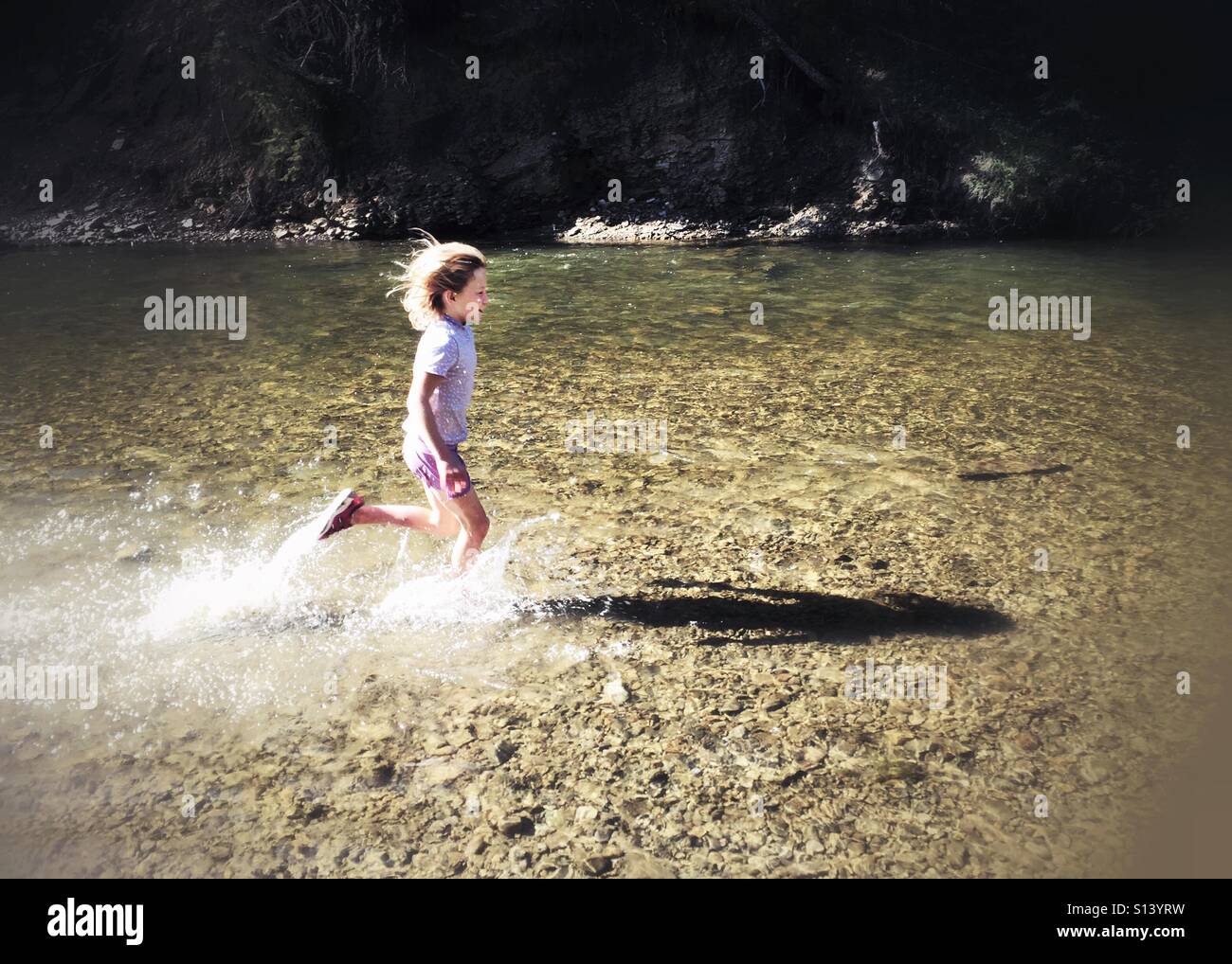 Water splashes as a child runs through a creek on a summer afternoon. - Smartphone Captured Stock Image
