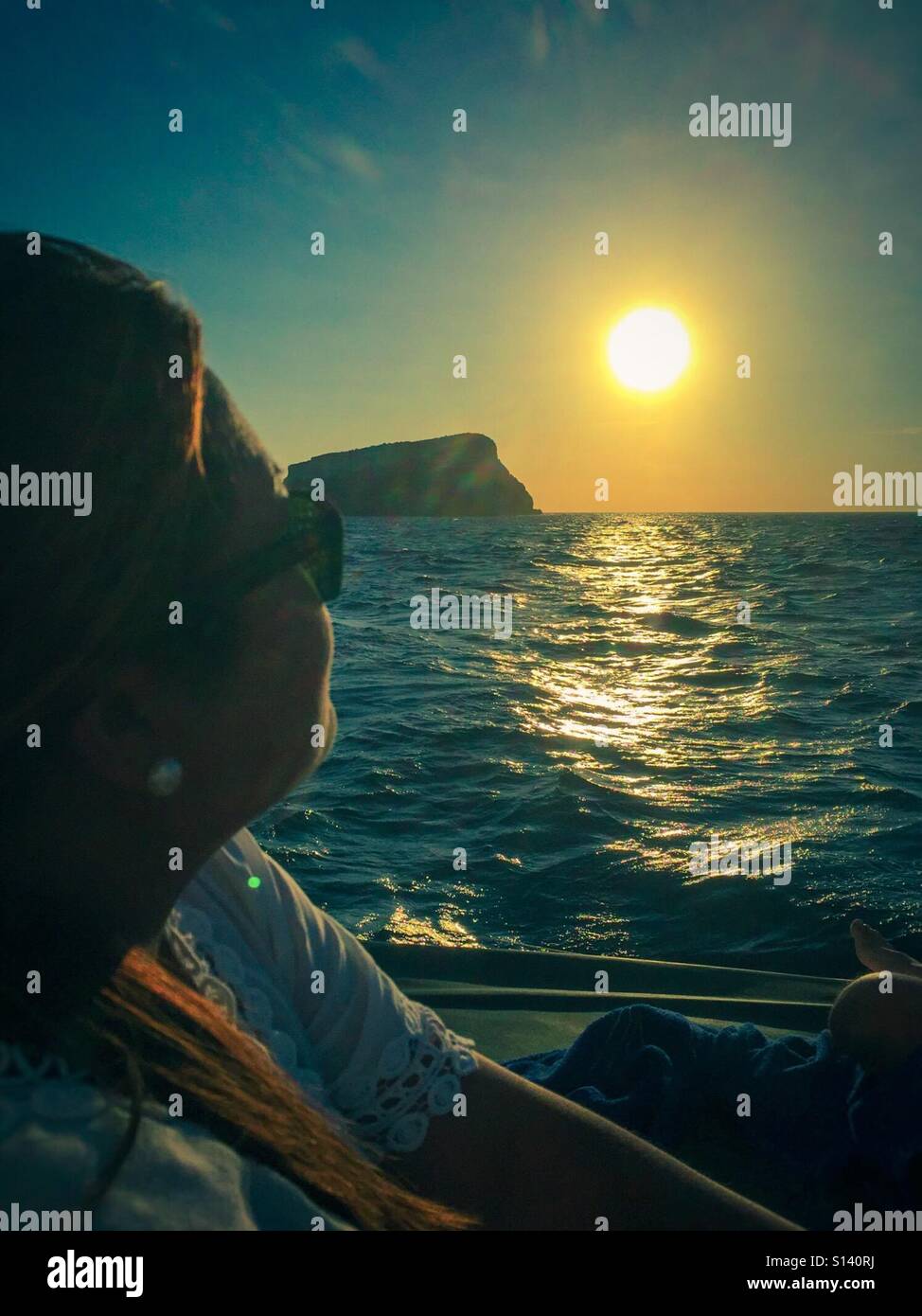 A lady on a boat sits and watches the sun set behind the Aegean Sea off the coast of Santorini. - Smartphone Captured Stock Image