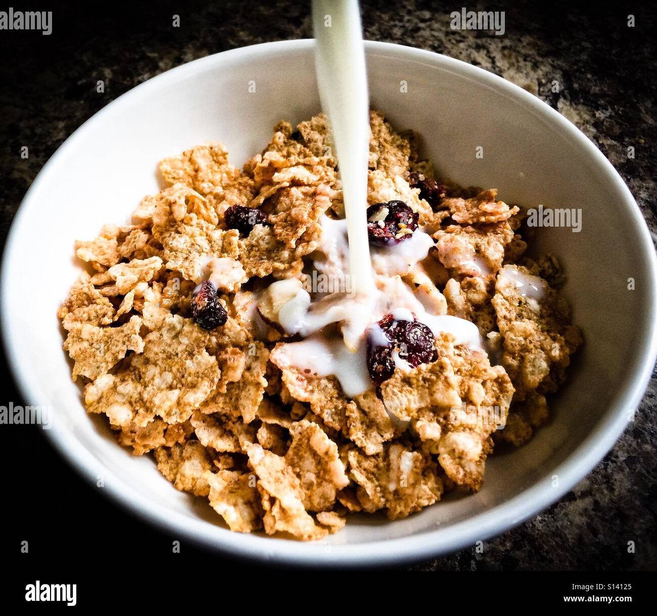 Milk pouring into a bowl with cereal flakes and dried fruit. - Smartphone Captured Stock Image