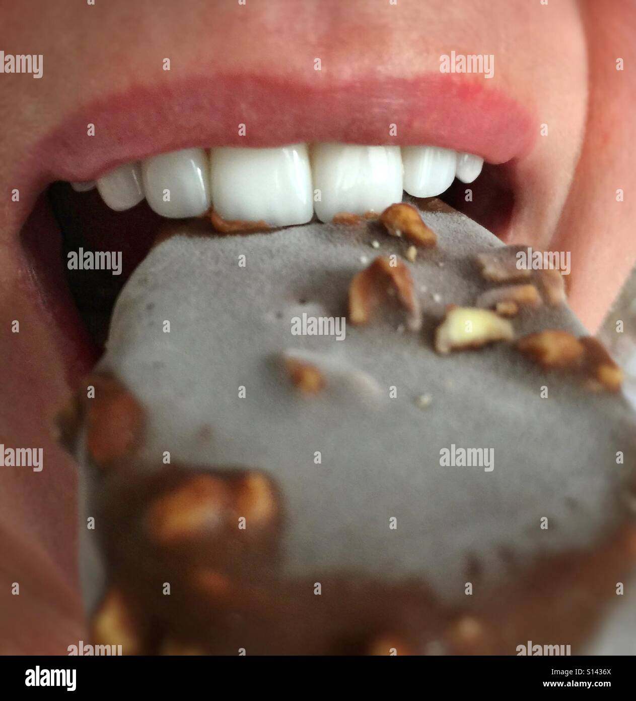 A close up of a mouth biting into an ice cream on a stick Stock Photo